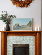 Wooden mantelpiece with a landscape painting of sea stacks by Leo Stafsnes, candles, and decorative leaves above.