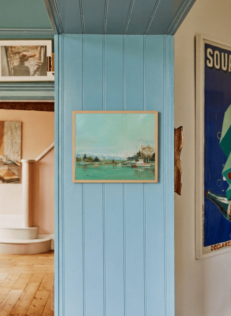 Room interior with a blue paneled wall, framed artwork by Leo Stafsnes, and a poster.