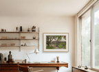 Home office with a desk, chair, and framed artwork by Leo Stafsnes on a wall.