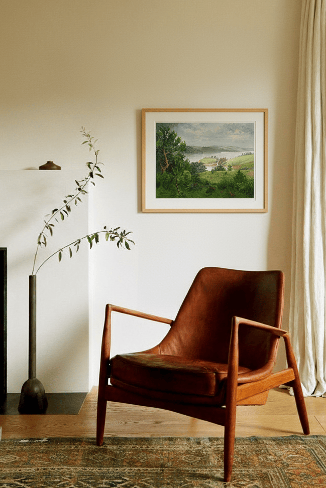 Brown leather chair in a room with a framed print by Leo Stafsnes on the wall and a curtain.